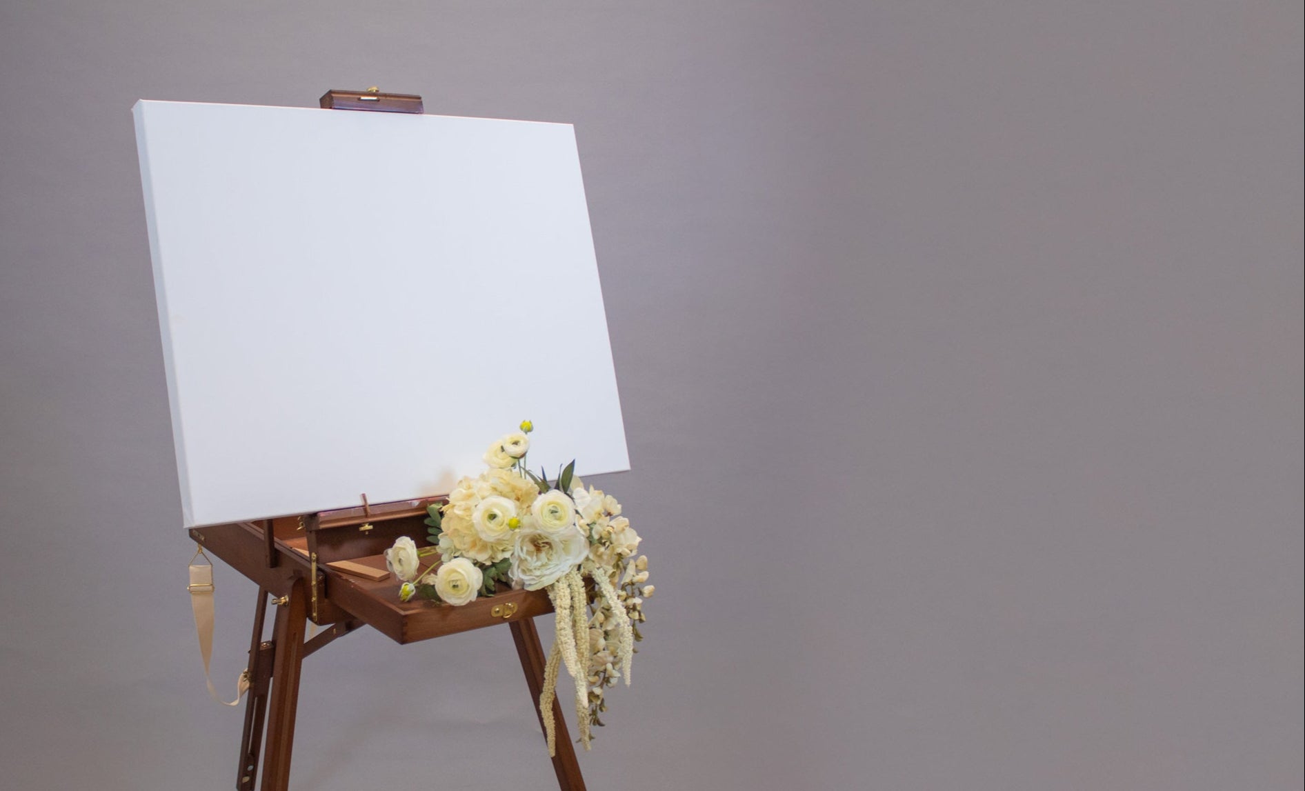 Wooden artist's easel with a blank white canvas against a gray background