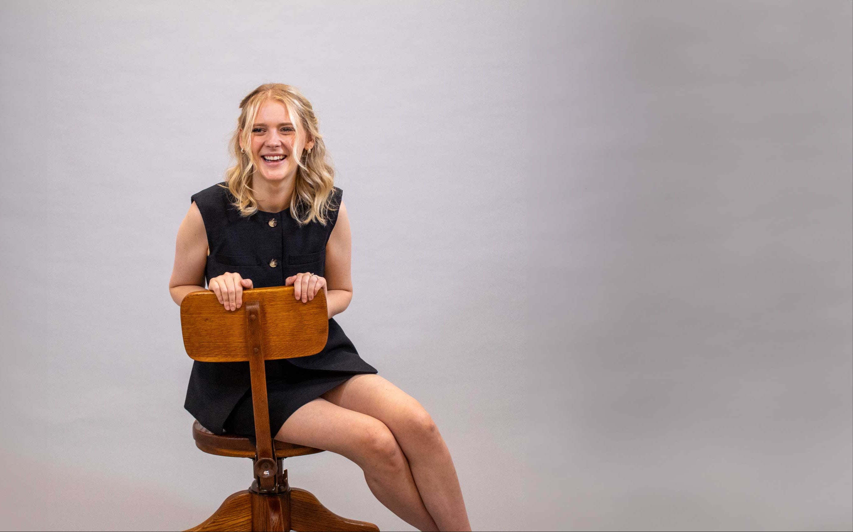 Woman sitting on a wooden stool against a plain background